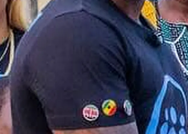 Close-up of country flag pins worn on the sleeve of a Them2Us mission shirt